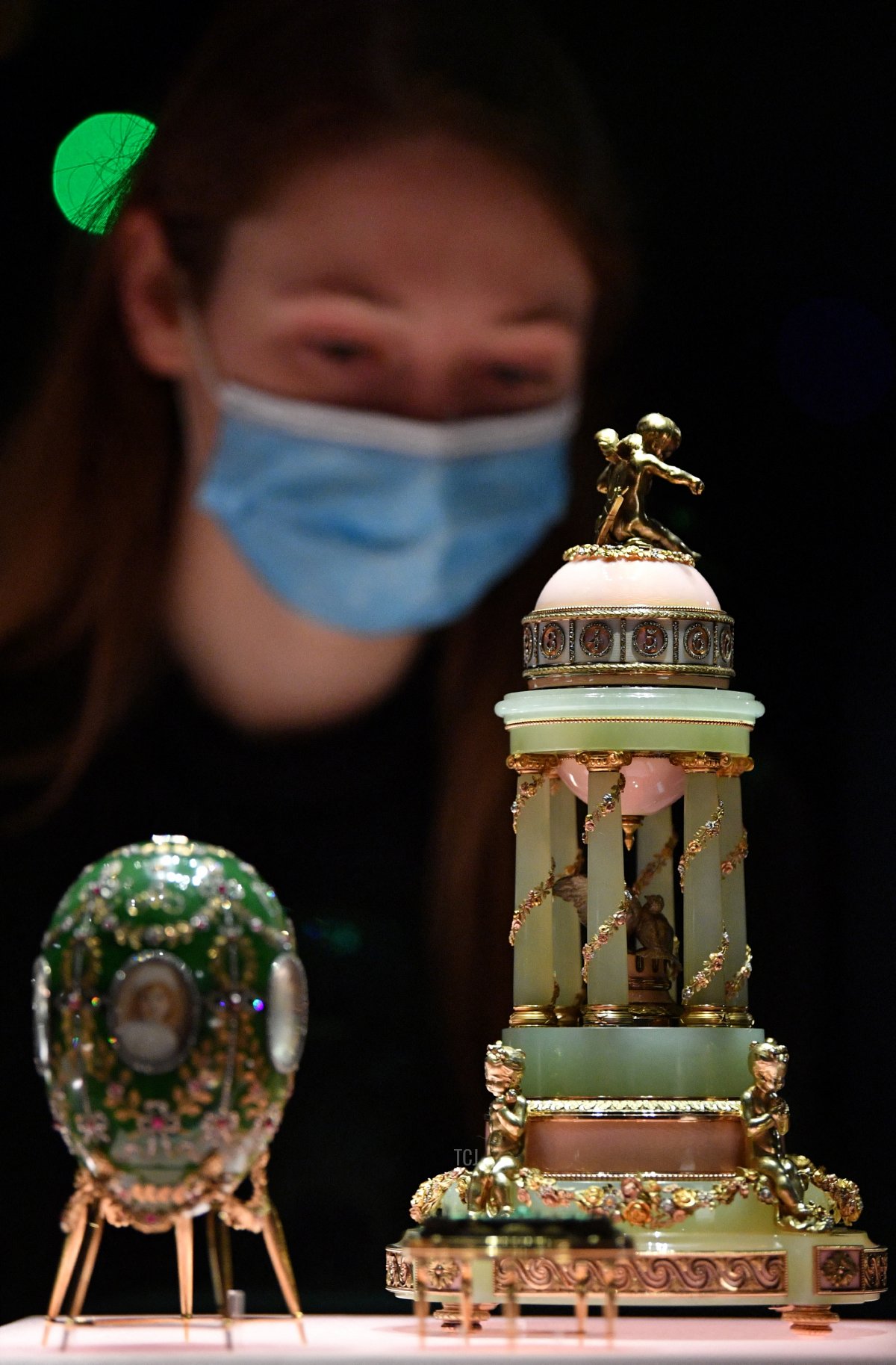 Un assistente alla galleria posa con l' 'Uovo Palazzo di Alessandro' (L) e l' 'Uovo Colonnade' durante una photocall per presentare l'esposizione 'Fabergé a Londra: Amore e Rivoluzione', presso il museo V&A (Victoria e Albert) di Londra il 17 novembre 2021