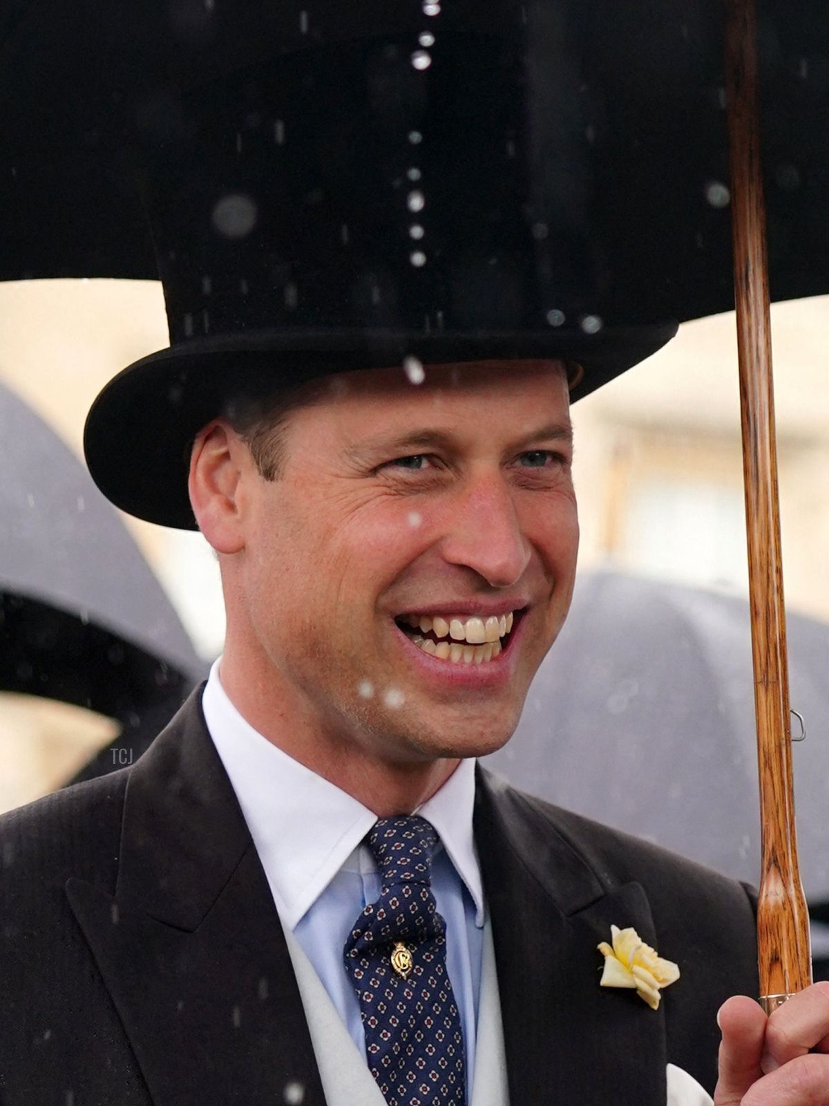 Britain's Prince William, Duke of Cambridge shelters from the rain beneath an umbrella as he meets guests at a Royal Garden Party at Buckingham Palace in London on May 25, 2022