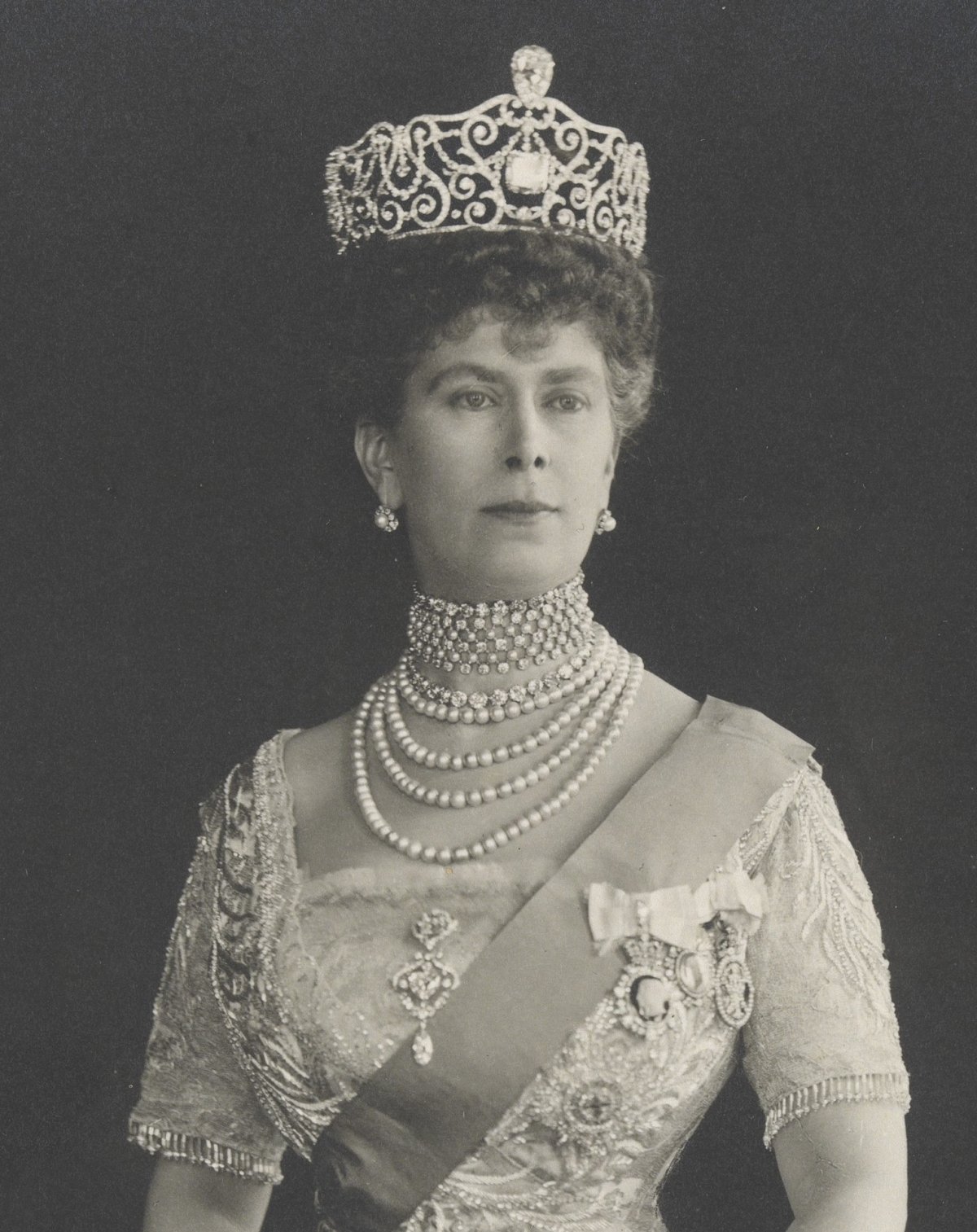 Queen Mary (May of Teck) standing, wearing the Delhi Durbar Tiara, including the Cullinan III (top) and Cullinan IV (center) diamonds, and holding a folded fan. The Delhi Durbar Tiara was created in 1911 and modified to accommodate the Cullinan stones in 1912