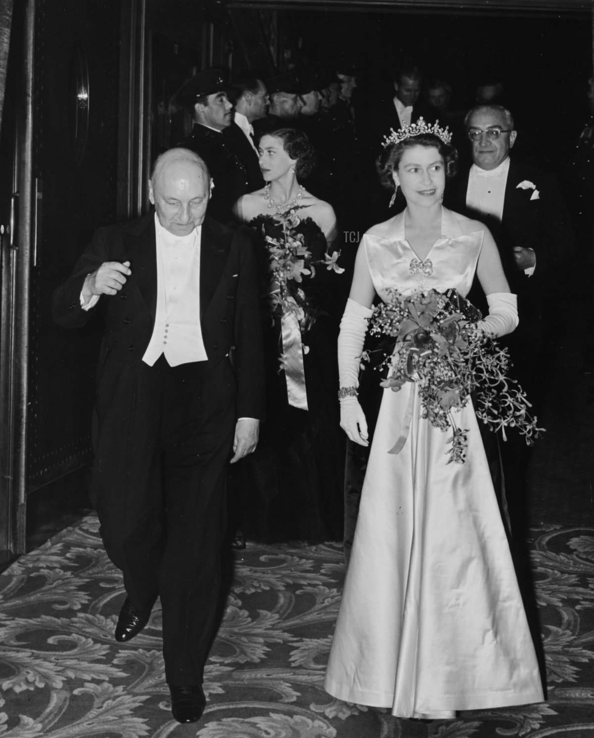 La regina Elisabetta II è scortata da Reginald Bromhead, presidente del Cinematograph and Trade Benevolent Fund, mentre lei e la principessa Margaret (dietro) lasciano la proiezione reale del film a Leicester Square, Londra, 27 ottobre 1952