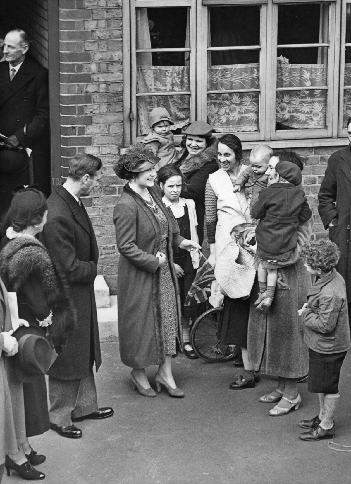 Re Giorgio VI e Regina Elisabetta a Londra, 1938. Re Giorgio VI (2° da sinistra) e Regina Elisabetta (3° da sinistra) visitano i quartieri poveri a Sud di Londra. Qui in conversazione con i residenti della McManus House a Battersea. Data creata: 16/03/1938