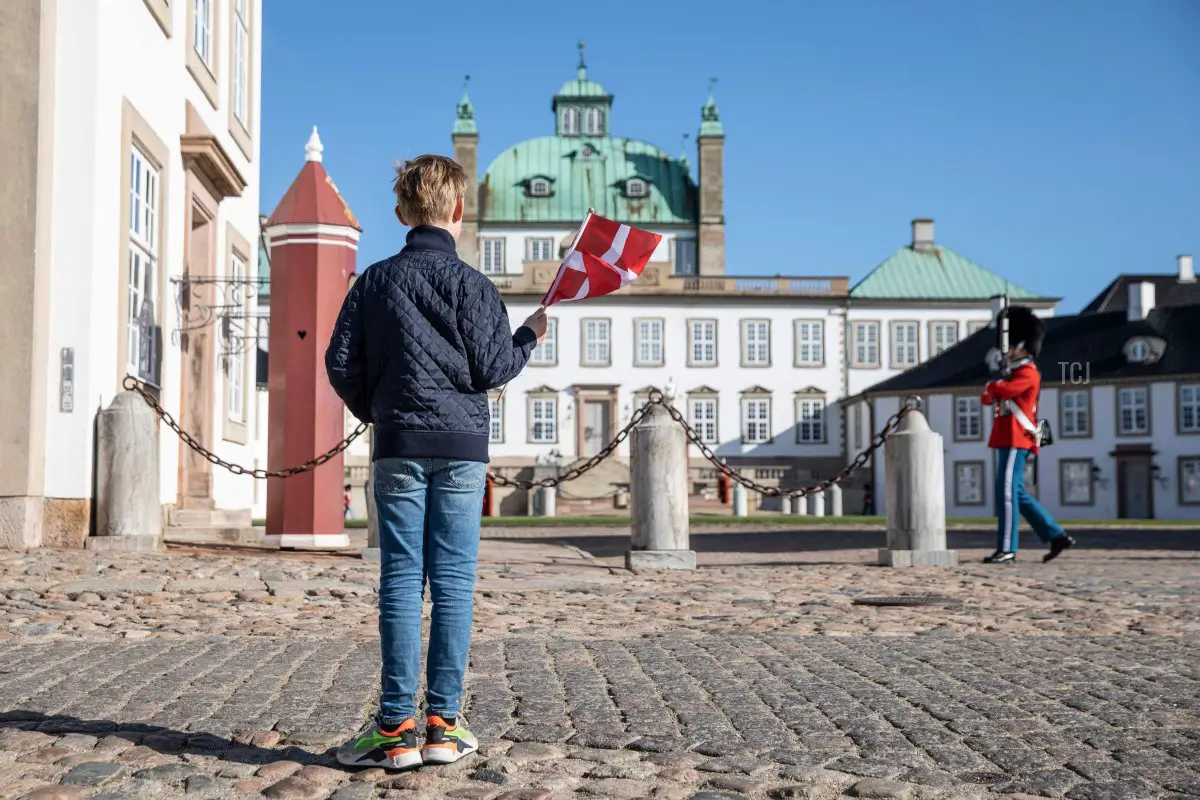 Un ragazzo saluta con una bandiera danese di fronte al Palazzo di Fredensborg il 16 aprile 2020, per l'80° compleanno della Regina Margrethe II di Danimarca, che celebrava in privato a causa della pandemia da coronavirus (OLAFUR STEINAR GESTSSON/Ritzau Scanpix/AFP via Getty Images)