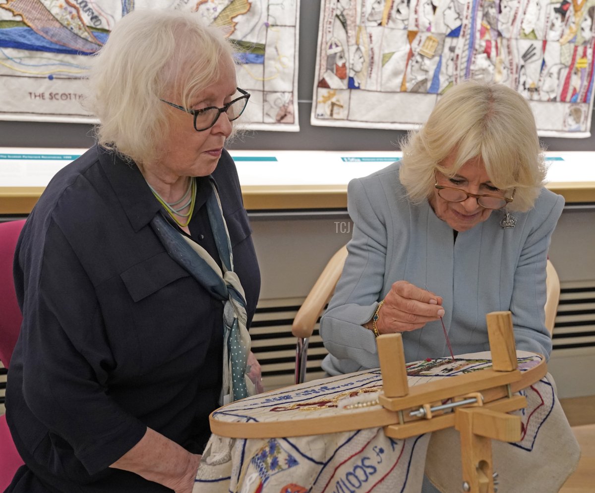 La coordinatrice delle ricamatrici del Great Tapestry of Scotland Dorie Wilke osserva la Regina Camilla mentre lavora su un arazzo commemorativo durante la sua visita al centro visitatori del Great Tapestry of Scotland a Galashiels, nei confini scozzesi, il 6 luglio 2023 (Andrew Milligan - PoolGetty Images)