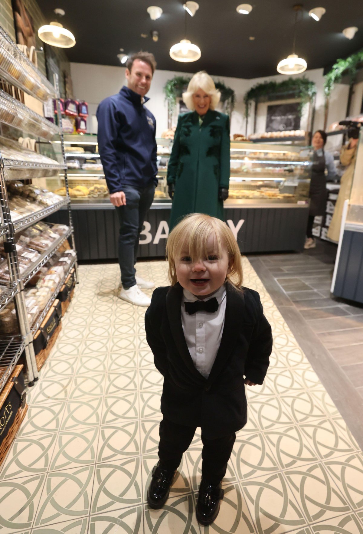 Queen Camilla of the United Kingdom meets the owner of Knotts Bakery, William Corrie, and his son Fitz during a visit to Lisburn Road in Belfast on March 21, 2024 (Liam McBurney/PA Images/Alamy)